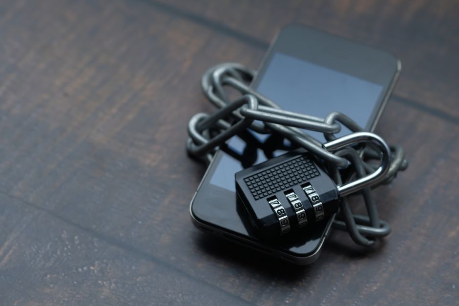 Close-up of a smartphone wrapped in a chain with a padlock, symbolizing strong security.